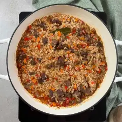 Arroz con carne y verduras, cocinado en una olla blanca. Los trozos de carne se mezclan con el arroz y pimientos rojos y zanahorias picadas.