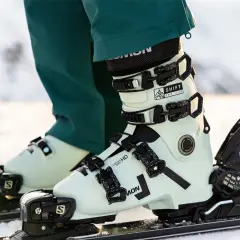Jasne, jasne buty narciarskie Salomon z czarnymi klamrami na nartach.