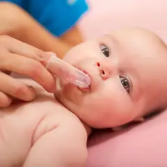 Delikatne pędzlowanie jamy ustnej niemowlaka specjalną nakładką na palec.
