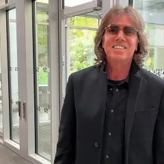 Joey Tempest, med sitt karaktäristiska hår och solglasögon, poserar framför en glasdörr.