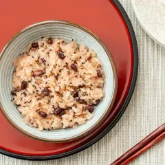 A bowl of Japanese red bean rice, sprinkled with black sesame seeds, sits on a red tray.