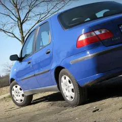 Niebieski Fiat Albea na tle drzew i błękitnego nieba.