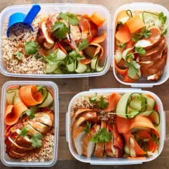 Vier Behälter mit braunem Reis, geschnittenem Hähnchenbrustfilet in Sauce, Gurken- und Karottenstreifen. Perfektes pre workout meal für unterwegs.