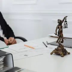 Prawnik omawia dyspozycję na wypadek śmierci w kilku bankach. Na biurku Statua Temidy, dokumenty i laptop.