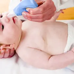 Pomoc w walce z katarem u niemowlaka. Ręce delikatnie trzymają dziecko, a niebieski aspirator do nosa jest używany do oczyszczania jego noska.