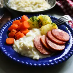 En blå tallrik med stuvad blomkål, kokt potatis, morötter och stekt falukorv. En klassisk svensk middag.