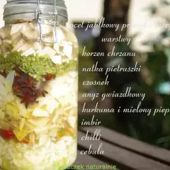 Słoik z warstwami składników do oxymelu: jabłko, chrzan, natka, czosnek, anyż, kurkuma, imbir, chilli, cebula.