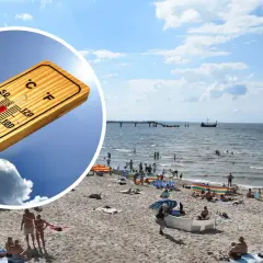 Słoneczna plaża, ludzie kąpią się w morzu. Termometr pokazuje wysoką temperaturę, idealna pogoda na majówkę nad morzem.