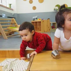 Bebés explorando en una **montessori guarderia**. Un niño gatea con un suéter rojo, mientras otro sonríe.