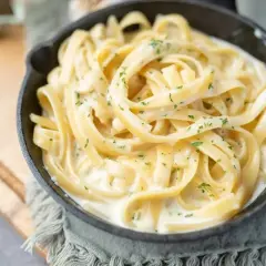 Kremowy makaron fettuccine w sosie śmietanowym, posypany natką pietruszki. Idealny pomysł, z czym zrobić makaron na szybko.