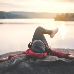 Kobieta odpoczywa na skale nad jeziorem, ciesząc się spokojem. To idealny moment na dodatkowy urlop i relaks.