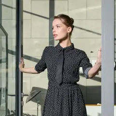 Elegancka sukienka w kropki z krawatem – idealna na imprezę firmową. Kobieta wchodzi przez szklane drzwi.