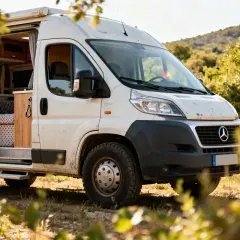 Un camping-car blanc, prêt pour l'aventure, avec sa porte ouverte révélant un intérieur cosy. Ce véhicule de marque camping car est garé en pleine nature.