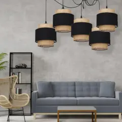 Pięcioramienna lampa pająk boho z abażurami z plecionki i czarnego materiału nad szarą sofą.