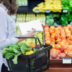 Donna con lista della spesa sceglie verdure fresche e frutta colorata al supermercato.