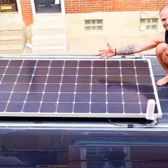 Hombre muestra cómo conectar dos placas solares en el techo de una furgoneta.