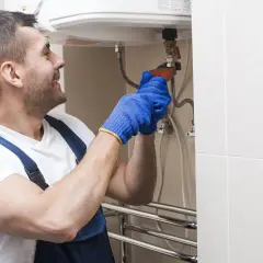 Fachowiec w niebieskich rękawiczkach dokręca zawór, pokazując, jak spuścić wodę z bojlera.