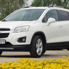 Biały Chevrolet Trax jedzie po drodze, otoczony żółtymi kwiatami.