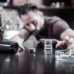 Mężczyzna z papierosem w popielniczce, butelki i kieliszek na stole. Czy wódka podnosi cukier?