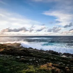 O mar bravo bate nas rochas rochosas, espumando e rugindo. O céu azul com nuvens brancas paira sobre o vasto oceano, um cenário perfeito para o portiño.