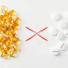 Kapsułki z omega-3 i tabletki z aspiryną, rozdzielone czerwonym krzyżykiem. Unikaj łączenia omega-3 z aspiryną.