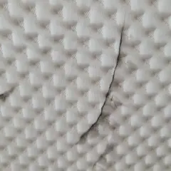Biała tkanina z pikowanym wzorem i ciemnymi smugami.