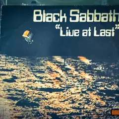 Okładka płyty "Black Sabbath 'Live at Last'". Widok z lotu ptaka na pustynny krajobraz, z małym pojazdem unoszącym się w powietrzu.