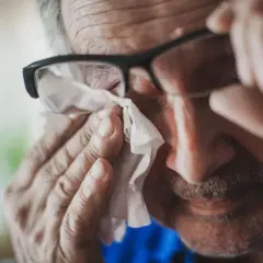 Starszy mężczyzna w okularach wyciera łzę chusteczką. Może to być objaw smutku lub reakcja alergiczna, np. na peritol.