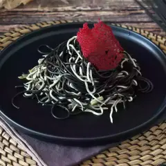 Spaghetti neri e bianchi, un contrasto elegante. Il nero di seppia dona un sapore unico a questo piatto, guarnito con una cialda rossa croccante.