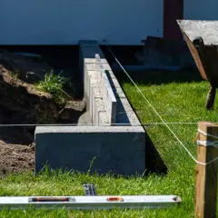 Budowa solidnego, jak głęboki fundament pod ogrodzenie. Widać betonowe bloczki, poziomicę i sznur geodezyjny.