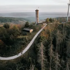 Radfahrer auf einem Weg zum Aussichtsturm Bergneustadt. Der Turm thront über einer bewaldeten Hügellandschaft.