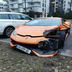 Pomarańczowe lambo po wypadku, przód mocno zniszczony. Obok białe kombi.
