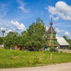 Zielona cerkiew, symbol tradycji starowierców w Polsce, na tle błękitnego nieba z chmurami. Bociany w gnieździe na słupie.