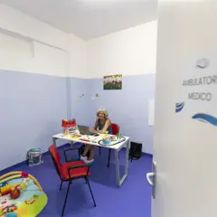 Un ambulatorio medico con una donna al computer, giocattoli e un tappeto gioco. La differenza tra ambulatorio e poliambulatorio è la specializzazione.