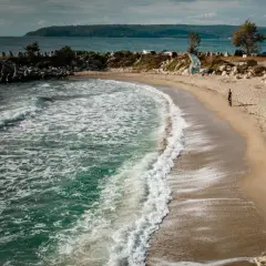 Plaża w Bułgarii, gdzie morze szumi, a fale obmywają brzeg. W oddali widać wzgórza i samochody.