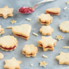 Sterne und Herzen aus veganen Keksen mit Marmeladenfüllung, dekoriert mit glitzernden Sternen.