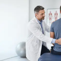 Medico esamina la schiena di un paziente, illustrando la differenza tra fisiatra e ortopedico.