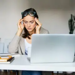 Kobieta z bólem głowy przy laptopie. Czy to znak, że sennik nowa praca przepowiada stresujące wyzwania?