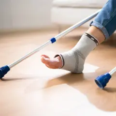 Osoba w ortezie na stawie skokowym próbuje chodzić z kulami. Rehabilitacja po artrodezie stawu skokowego wymaga cierpliwości.