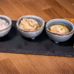 Tre skålar med dipp, en med dill, och två med en smak av 7 kryddor, serveras med rostat bröd på en stenplatta.