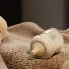 Butelka Avent z mlekiem i pluszowe owieczki na kocyku.