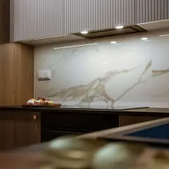 Elegancka kuchnia z drewnianymi frontami i płytkami z subtelnym marmur wzór. Na blacie deska z warzywami.