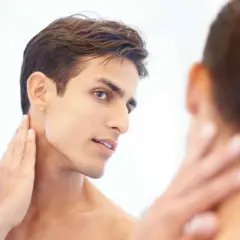 Un homme au visage fin et à la mâchoire marquée, la main caressant son cou, révélant une belle v line.