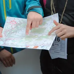 Dłonie wskazują trasę na mapie podczas biegu na orientację.