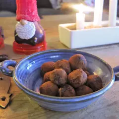 En blå skål med chokladpraliner, perfekta som julgodis utan socker. I bakgrunden syns tomteljus och adventsljusstake.