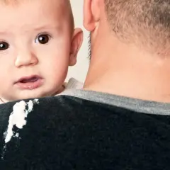 Un neonato di 1 mese ha un rigurgito, lasciando una macchia sul maglione del padre.