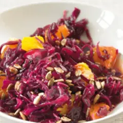 Rotkohlsalat mit Apfel und Orange, garniert mit Sonnenblumenkernen, in einer weißen Schüssel.