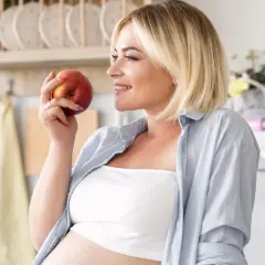 Kobieta w ciąży trzyma jabłko, zastanawiając się, co jeść żeby zajść w ciążę. Zdrowa dieta to podstawa.