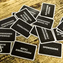 Karty do gry "Czółko" online leżą na drewnianym stole. Zadania na kartach to m.in. "Opowiadanie śpiewając", "Pokazywanie z dłonią na głowie", "Naśladowanie dźwięków".