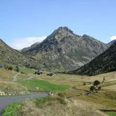 Un camino serpentea hacia el estany de Juclar, un valle andorrano con casas dispersas y un pico imponente.